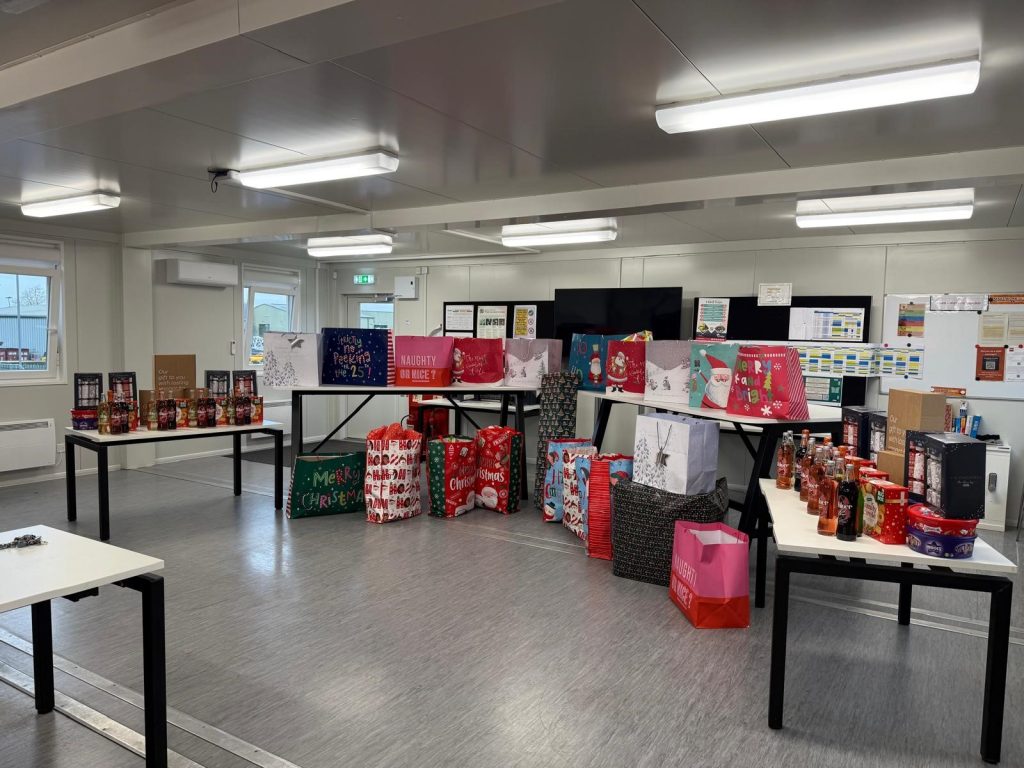 A large amount of Christmas wrapped presents and bags on a table.